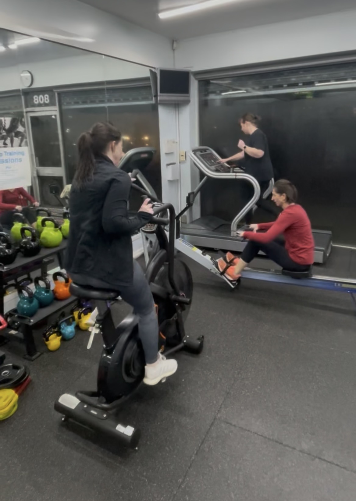 Three clients training together in the private studio — on the bike, treadmill and rower