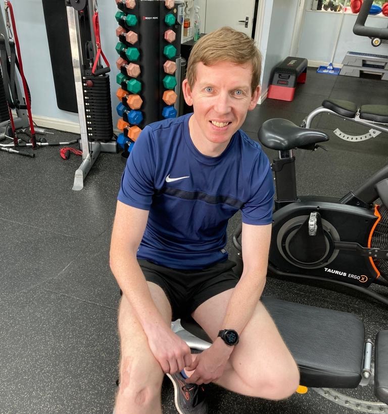 Mathew Heckford, personal trainer in Didsbury, seated on a gym bench in the studio